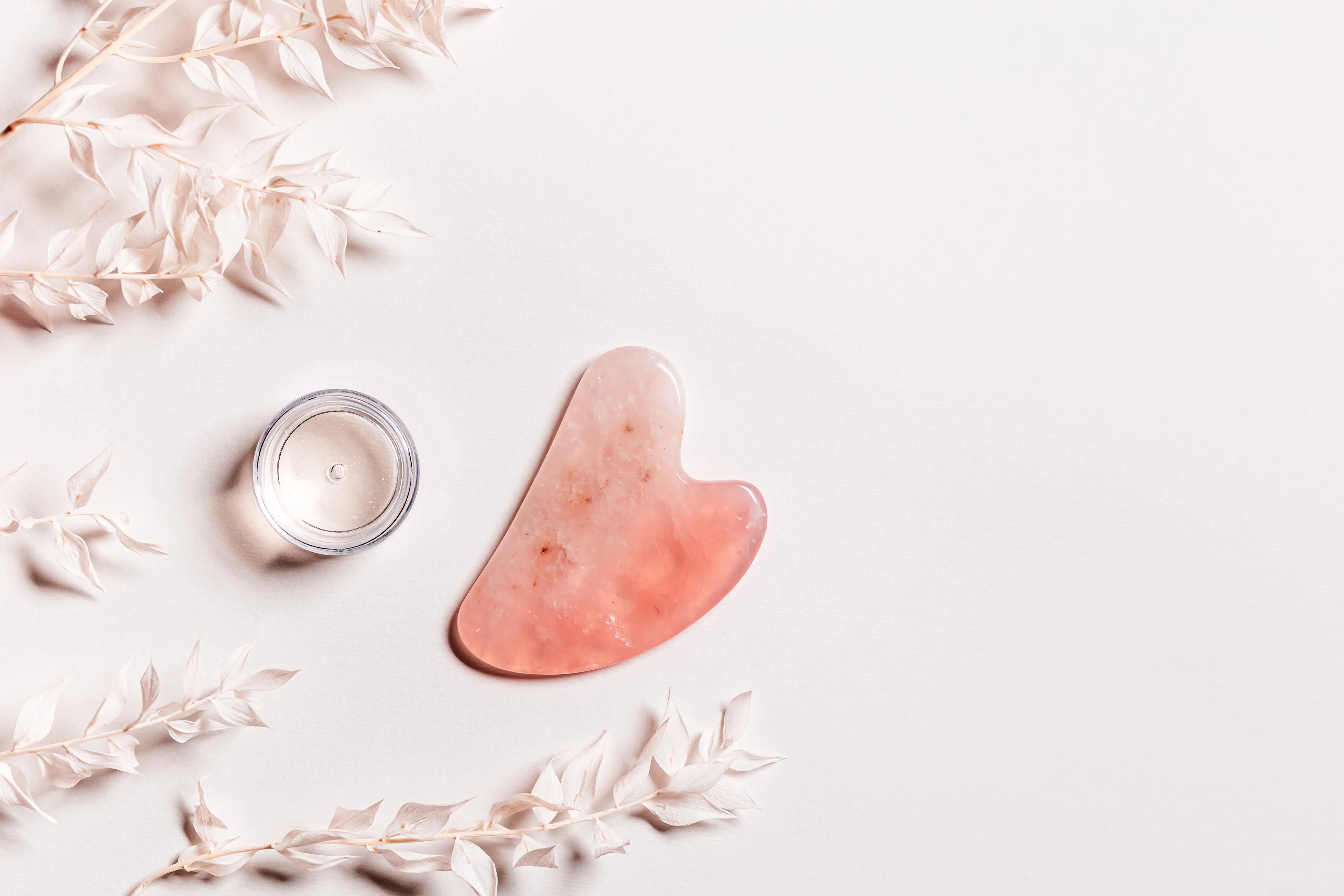 guashe-scrapes-from-rose-quartz-cosmetic-product-bottle-cream-natural-stone-massager-face